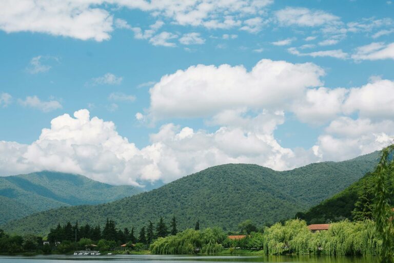 Green ridges near lake under blue cloudy sky