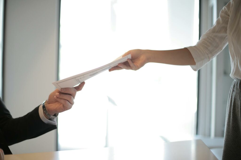 Close-up of hands exchanging documents in a business setting indoors.