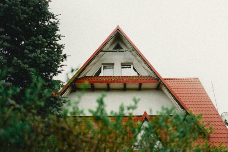 Charming house with a distinct red triangle roof surrounded by greenery, showcasing unique architecture.